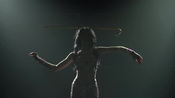 Young Arabian Belly Dancer in Exotic Dance Holding a Golden Cane on His Head, Shot in a Dark Studio