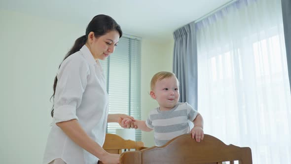 Caucasian loving mom play with cute baby boy child on bed in bedroom in the morning at house.