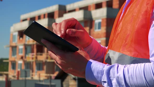 Construction Worker Works on the Tablet in Front of Building Site - Closeup of Tablet