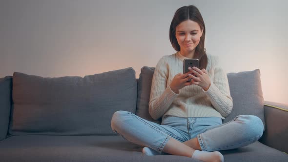 Smiling Young Woman Using Smartphone Texting Message Sit on Couch, Using Social Media, Browsing