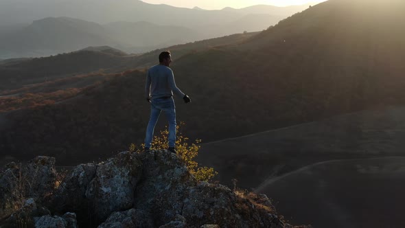 A Man Rejoices in Life Standing on Top of a Cliff Against a Backdrop of Mountain Slopes and Valleys