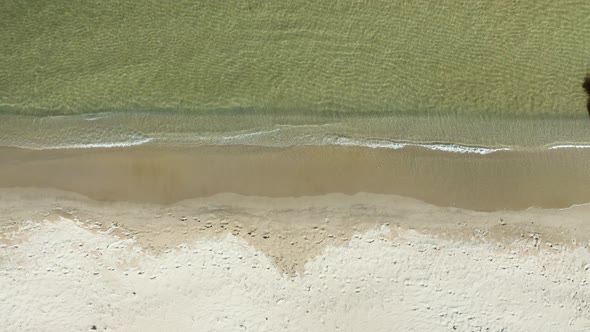 Empty beach with calm waves and crystal clear water, drone top down