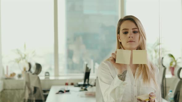Young Businesswoman Sticking Sticky Notes on Glass at Office