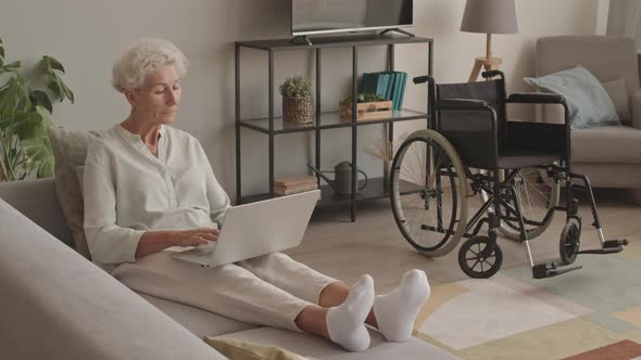 Senior Woman Sitting on Sofa with Laptop