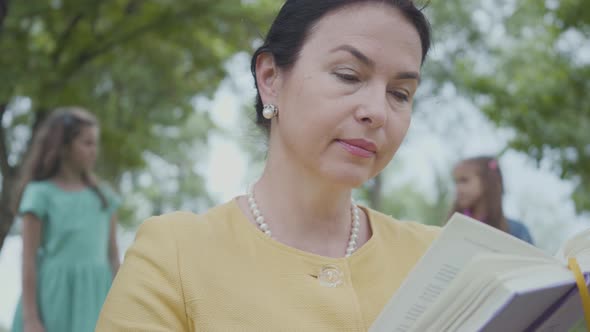 Portrait of an Elegant Senior Grandmother Reading the Book in the Park in the Foreground