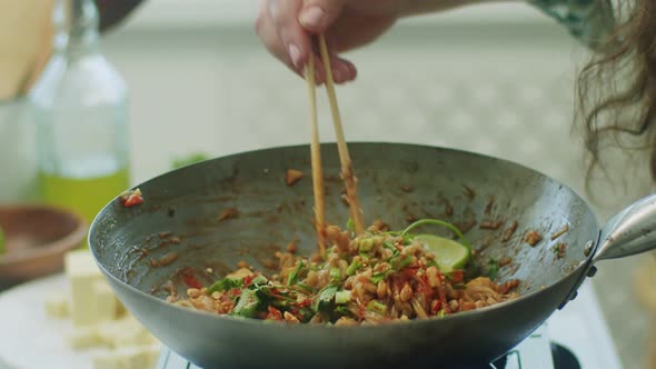 Woman mixing delicious wok noodles with chopsticks