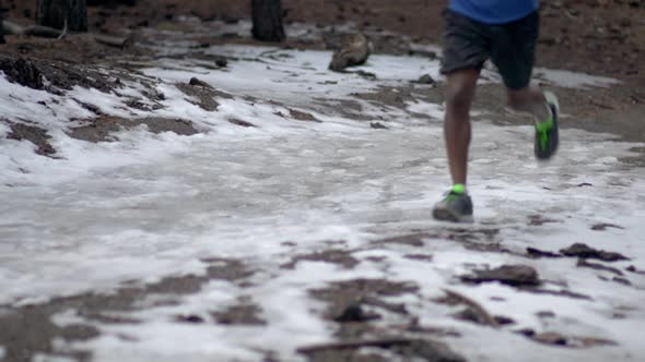 A young man trail running on a snow covered trail in a forest in the mountains.