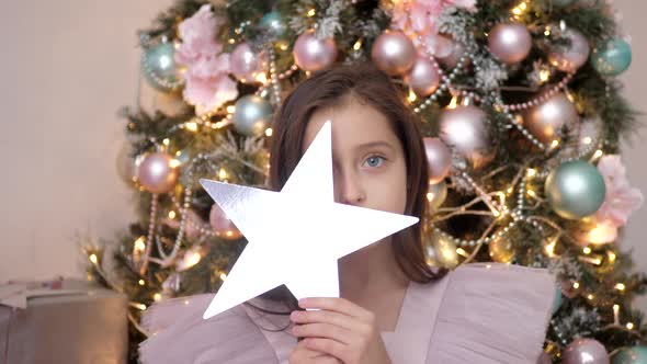 Beautiful Caucasian Girl Judges at the Christmas Tree in Pink Dress and Holds a Star