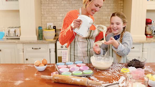 Smiling mother holding whisk while daughter playing with mixture 4K 4k