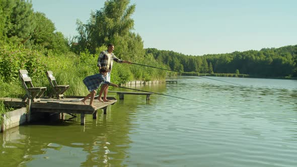 Joyful School Age Boy and Black Father Casting Fishing Rods From Jetty on Lake