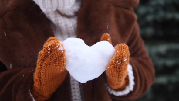 Female Hands In Knit Mittens Holding Heart Of Snow In Winter Outdoors.