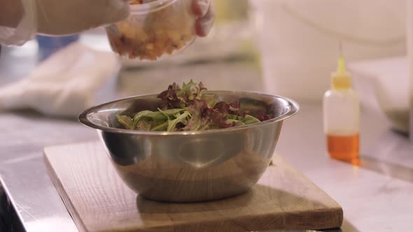 Restaurant Cooking  Chef Adds Pumpkin Pieces to Lettuce Leaves in a Bowl