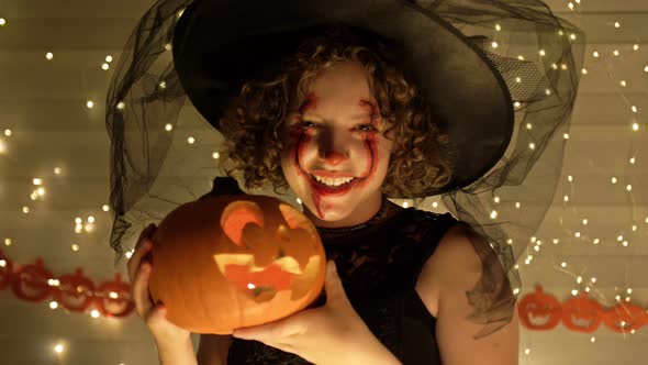 Portrait of a Teenage Girl Dressed As a Witch with Scary Makeup on Her Face, The Girl Holds a Jack-o