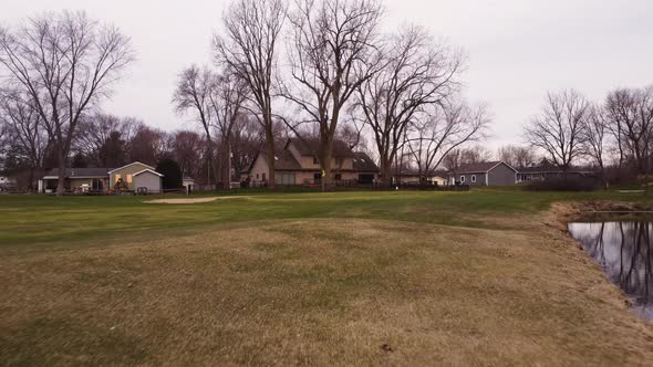 Golf course on an overcast day. Aerial shot moving forward on to the green, Trees and houses in the