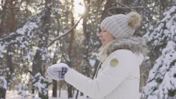 Side View Cute Girl in Warm Winter Clothes Throws Snow Up and Laughs Cheerfully