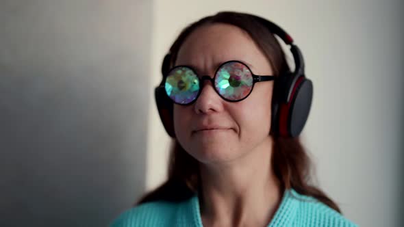 Crazy Lady with Funny Glasses is Listening to Music By Wireless Headphones Portrait Indoors