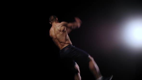 Young Pumped Man Runs Out of the Dark and Doing a Flip  Bright Lighting on the Background