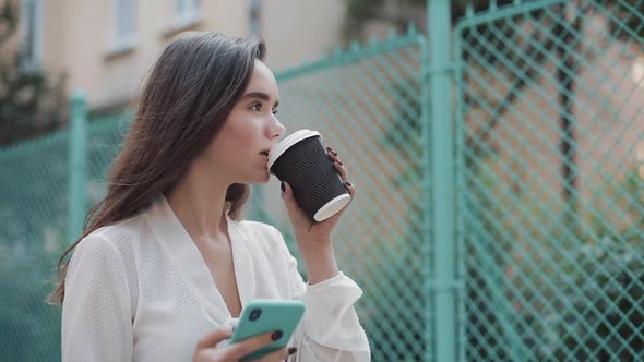 Pretty Young Smiling Brunette Girl Walking at Cosy Old Town Street While Using Her Phone and