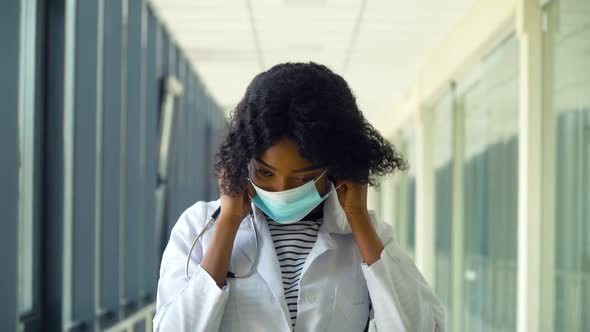 African American Female Doctor Puts on Medical Mask in Modern Clinic. Stop Virus