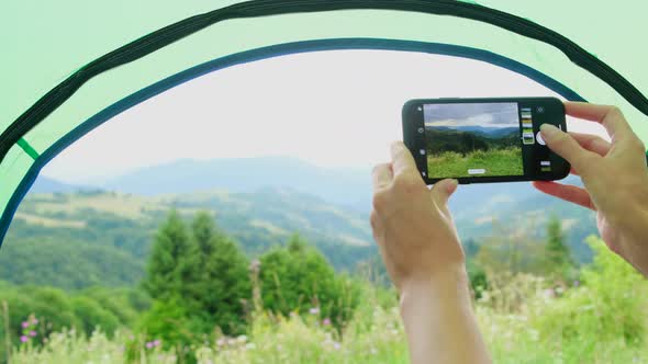 Girl Takes Pictures with a Smartphone of the Mountains From Her Tent Summertime