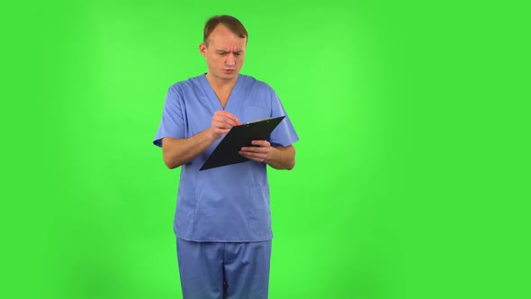 Annoyed Doctor Fills Papers at Black Folder with Pensil. Green Screen