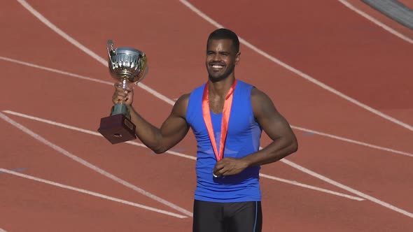 Muscular sportsman showing his medal and cup for victory to fans on stands