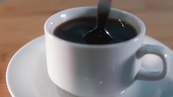 Close Interior Shot of Stirring Black Coffee With Metal Spoon at Night