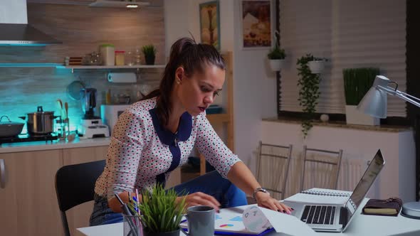 Woman Checking Notes on Clipboard Using Laptop