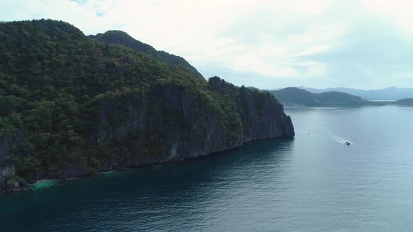 Dramatic aerial orbit of rocky islands with green vegetation in Palawan, Philippines. A boat passes