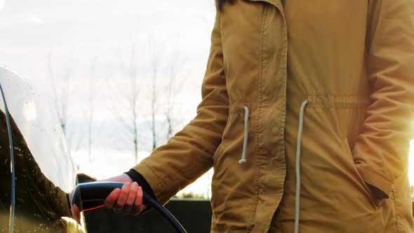 Woman charging the electric car on a winter day