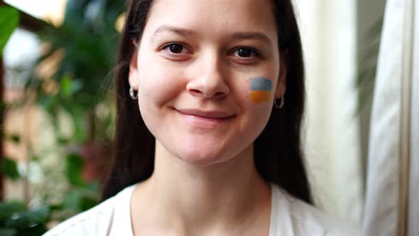 A Smiling Young Ukrainian Girl with the Flag of Ukraine on Her Face is Looking to Camera