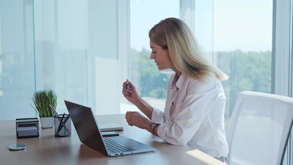 A Woman is Working on a Laptop Making Notes in Notebook in Office