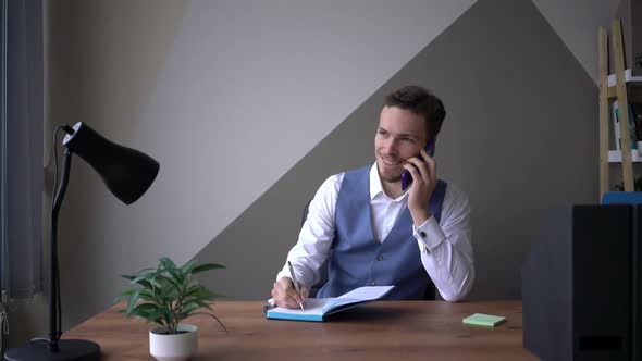 Handsome Male Office Manager Using Smartphone at Workplace Sitting on a Desk
