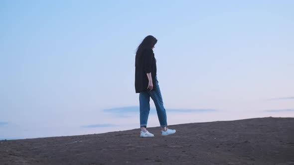 Business Woman with Dark Long Hair Walks Along Road Against Background of Beautiful Pink Sky at