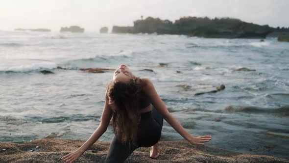 Girl Does Stretching Standing on Stone Against Waving Ocean