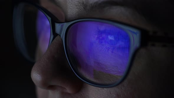 Closeup Portrait of a Caucasian Woman in Glasses Looks at the Screen with Graphs in the Dark