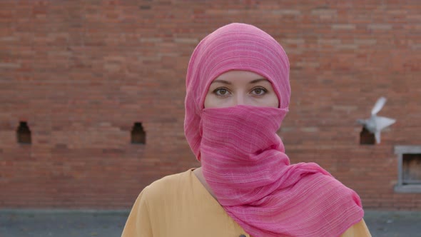 Attractive Muslim Woman with Natural Make Up Wearing Pink Hijab Scarf Looks at Camera