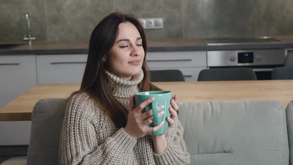 Closeup of Attractive Millennial Woman Sitting of Couch Looking Away and Drinking Coffee or Tea at