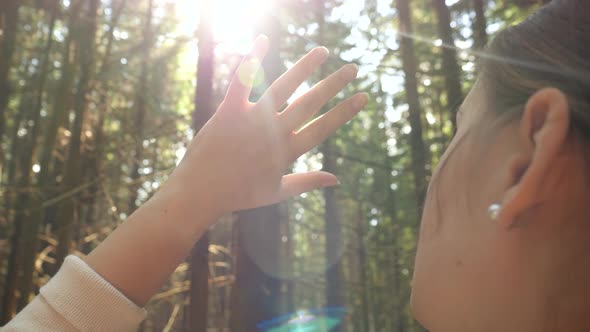 Beautiful Young Woman Looking on Bright Sun Through Her Fingers While Relaxing in Pine Forest at