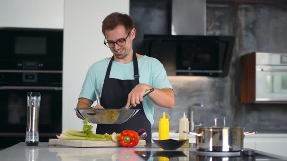 Portrait of Focused Young Man Chef Cook Tasty Dish in Pan at Modern Kitchen