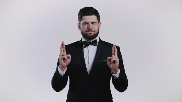 Young Caucasian Man Praying with Crossing Fingers Over White Background