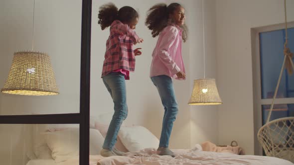 Playful Black Preadolescent Sisters Jumping on Bed