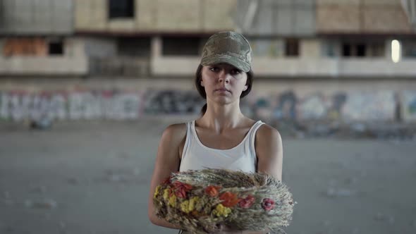 Portrait of a Beautiful Girl in a Camouflage Cap and White T-shirt Holding a Wreath