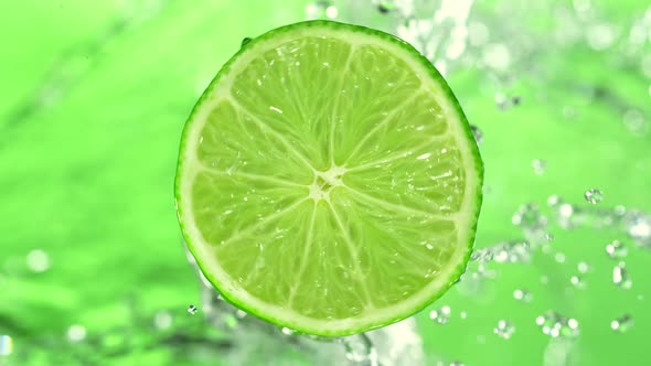 Super Slow Motion Detail Shot of Rotating Fresh Lime Slice and Splashing Water at 1000Fps