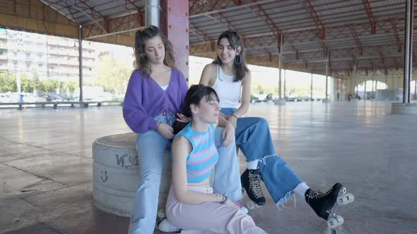 Three Girls Sit in Roller Skates and Talk As One Fixes Another’s Hair