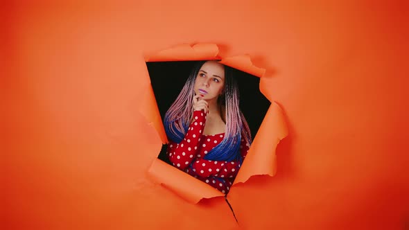 Thoughtful Young Woman Scratching Chin and Looking Out of Hole of Orange Background