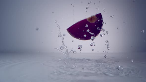 Halved red onion falling on water surface. Slow Motion.