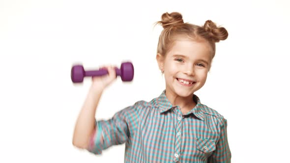 Small Active Caucasian Kid Girl in Plaid Shirt and Hair Buns Pushing Up Purple Dumbbell Smiling and