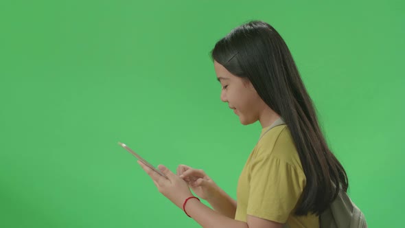 Side View Of Asian Girl Student Use Tablet And Walking To School On Green Screen Chroma Key