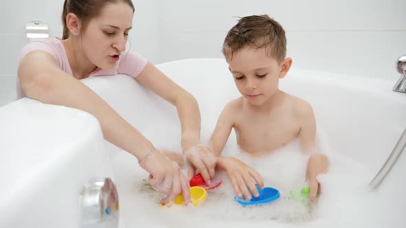 Smiling Mother Playing Toy Boats and Ships with Her Son Washing in Bath